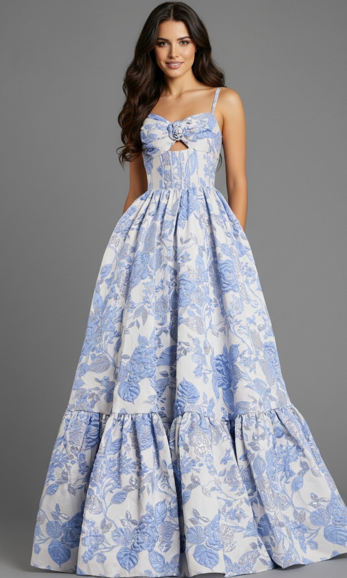 A woman stands against a gray background wearing the Jovani 47328 long prom dress—a floor-length, sleeveless white floral jacquard gown with a fitted bodice and a-line skirt.
